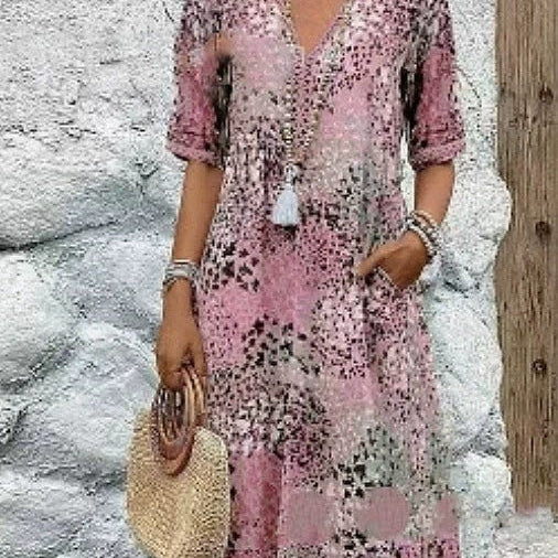 Woman wearing a pink floral dress standing against a stone wall.