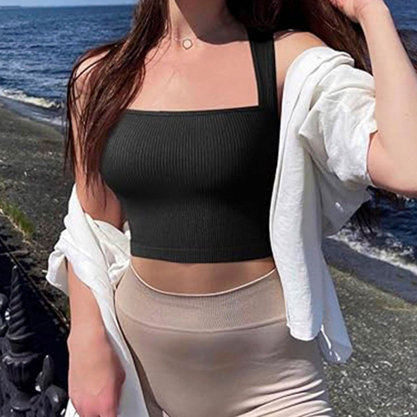 Woman in black crop top and beige pants standing on a beach.