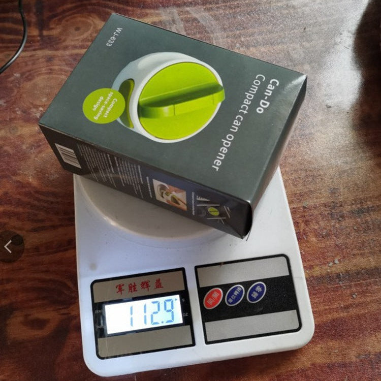 Box of a compact can opener on a digital scale with a wooden surface background