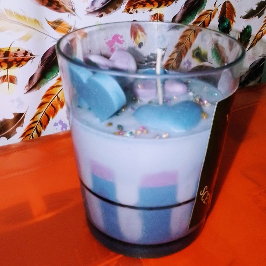 Candle in a glass holder with colorful wax on a floral-patterned surface
