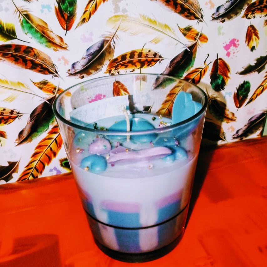 Glass with colorful liquid and candy on a red surface with feather-patterned fabric in the background