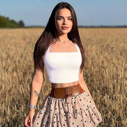 Woman standing in a field wearing a white top and polka dot skirt.