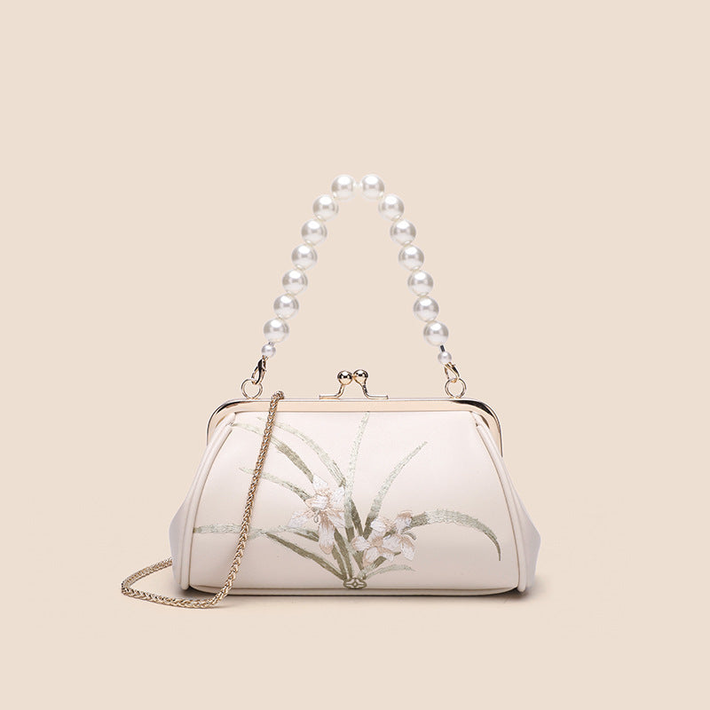 White handbag with floral design and pearl handle on beige background