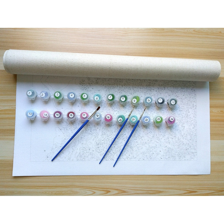 Set of small bottles with colorful labels and paintbrushes on a white paper roll against a wooden surface.