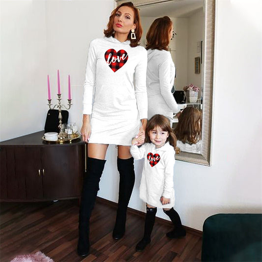 Woman and child wearing matching white sweaters with red heart designs in a room.