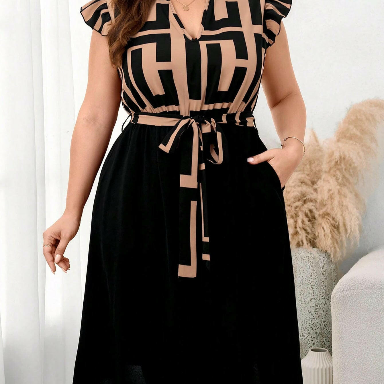 Woman wearing a black and beige patterned dress in a room with a white curtain and decorative items.