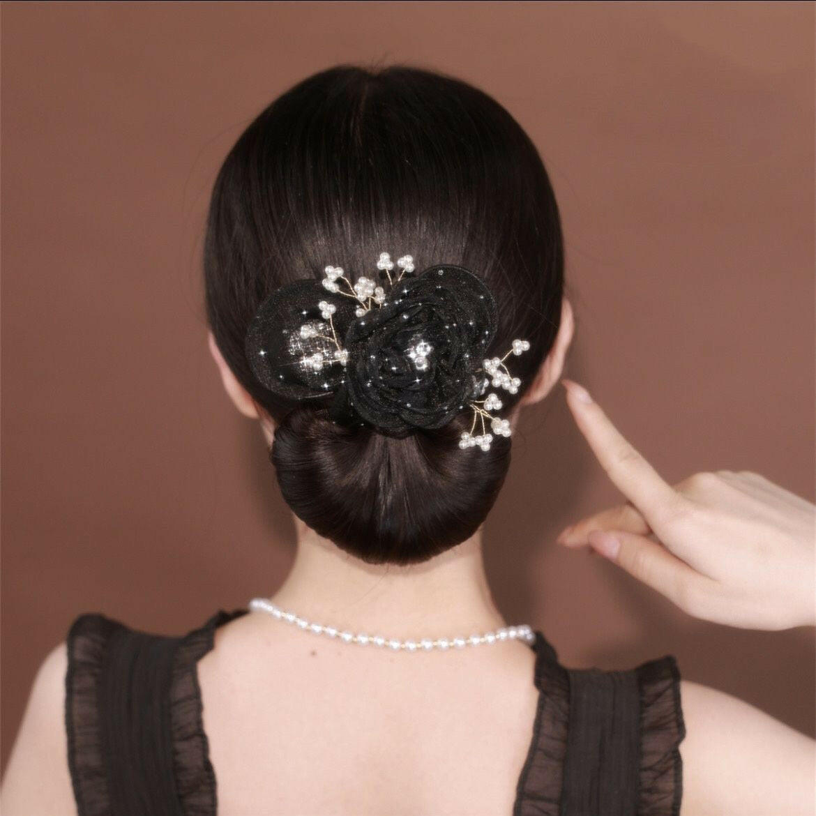 Woman with a decorative hair bun pointing to it against a brown background