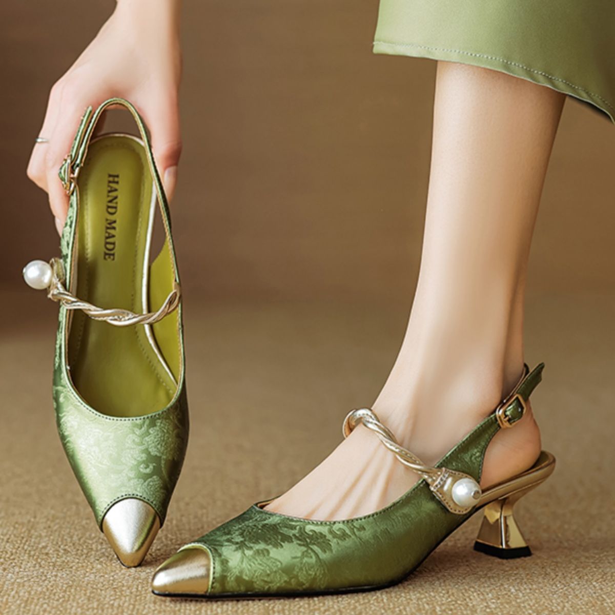 Green high-heeled shoes with pearl accents worn by a person on a brown background