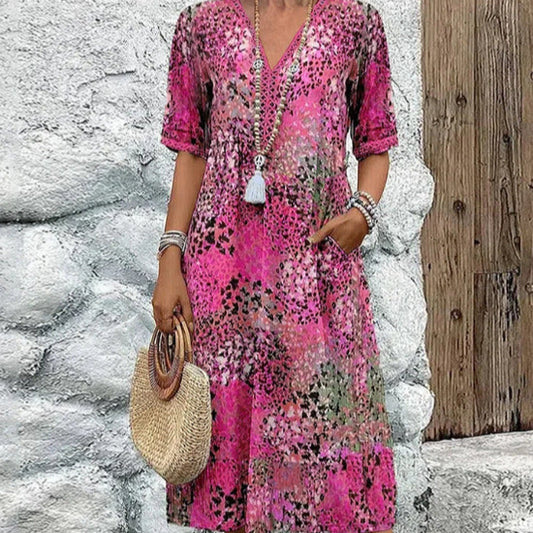 Woman wearing a pink floral dress holding a straw bag against a stone wall.